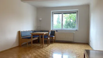 Helles Wohnzimmer mit Parkettboden, einer gemütlichen Sitzecke und Blick ins Grüne.