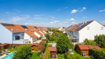 Luftaufnahme einer Wohnsiedlung mit Reihenhäusern, Gärten, Pool und Solaranlagen auf den Dächern.