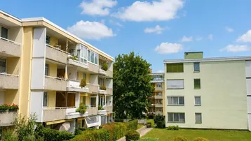 Mehrere Wohngebäude mit gepflegten Grünflächen und blauem Himmel an einem sonnigen Tag.