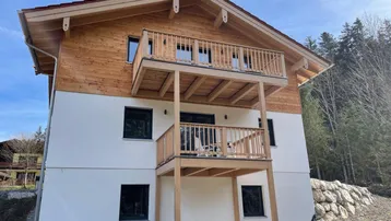 Modernes Holzhaus mit weißer Fassade und zwei Balkonen in alpiner Umgebung.
