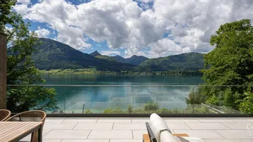 Geräumige Terrasse mit modernen Fliesen, bequemen Liegen und einem atemberaubenden Blick auf den See und die Berge.