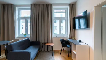 Heller Wohnbereich mit Sofa, Schreibtisch und Fernseher an der Wand.