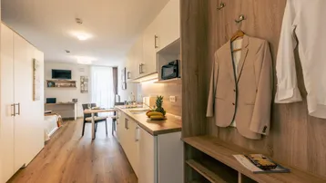 Moderne Einzimmerwohnung mit integrierter Küchenzeile, Essbereich und Garderobe am Eingang.