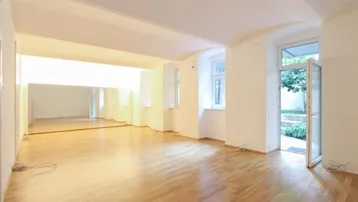 Großer, heller Raum mit Holzparkett, einer Spiegelwand und direktem Zugang zu einem kleinen Gartenbereich.