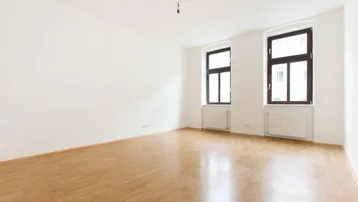 Helles, leeres Zimmer mit Parkettboden und zwei Fenstern, bereit zur individuellen Gestaltung.