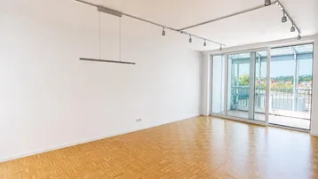 Helles, leeres Wohnzimmer mit Parkettboden, moderner Beleuchtung und Zugang zu einem verglasten Balkon.