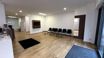 Moderner Empfangsbereich eines Büros mit Holzboden, Wartezone und Blick in weitere Arbeitsräume.