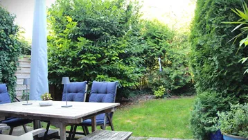 Gemütliche Terrasse mit Holztisch und Stühlen, umgeben von üppigem Grün und einem gepflegten Rasen.