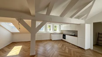 Heller offener Wohnbereich mit moderner Einbauküche, Fischgrätparkett und sichtbaren Dachbalken.