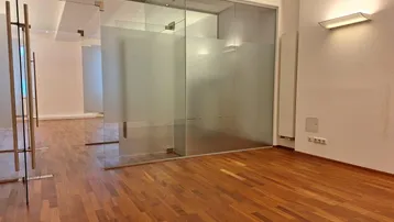Moderner Büroraum mit Holzboden und Glaswänden, die für Transparenz und Helligkeit sorgen.