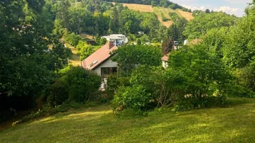 Malerischer Blick auf ein Haus inmitten einer grünen Hügellandschaft mit Weinbergen im Hintergrund.