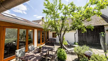 Sonniger Innenhof mit Holztisch, Stühlen und üppiger Bepflanzung, ideal für Mahlzeiten im Freien.