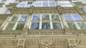 Detailaufnahme einer prunkvollen Fassade mit großen Fenstern und reich verzierten architektonischen Elementen.