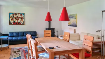 Geräumiger Wohn-Essbereich mit Holztisch, gemütlicher Sitzecke und einem traditionellen Kaminofen.