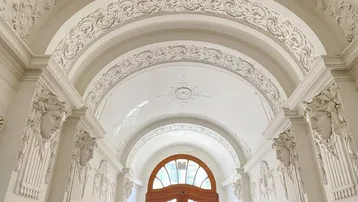 Elegante Eingangshalle mit aufwendigen Stuckverzierungen, hohen Gewölbedecken und Holztüren.