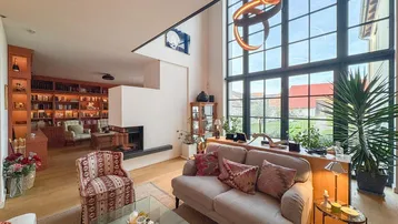 Geräumiges Wohnzimmer mit Kamin, hohen Decken und großen Fenstern, die viel Tageslicht hereinlassen.