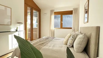 Helles Schlafzimmer mit Holzboden, Zugang zum Balkon und schräger Decke.