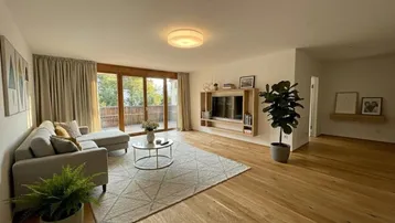 Helles Wohnzimmer mit Holzboden, gemütlichem Sofa und Zugang zu einem Balkon.