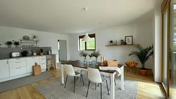 Moderne offene Küche mit Essbereich, weißen Schränken und Zugang zum Außenbereich.