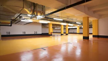 Geräumige Tiefgarage mit nummerierten Stellplätzen, gelben Säulen und sichtbaren Lüftungsrohren.