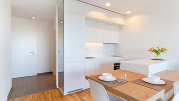 Moderne, helle Küche mit weißer Einbauküche, Holzboden und Essbereich in offenem Wohnkonzept.