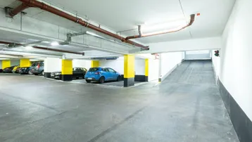 Helle Tiefgarage mit markierten Parkplätzen, gelben Säulen und einer Zufahrtsrampe.