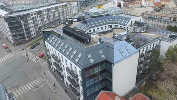 Luftaufnahme eines modernen Gebäudes in städtischer Umgebung mit Dachfenstern und Solaranlagen.