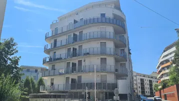 Modernes Mehrfamilienhaus mit geschwungenen Balkonen und heller Fassade unter blauem Himmel.