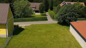 Luftaufnahme eines Baugrundstücks mit umliegenden Häusern und Fernblick auf die Stadt und Berge.