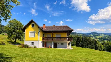 Gelbes Landhaus mit traditionellem Holzbalkon und weitem Blick über die grüne Hügellandschaft.