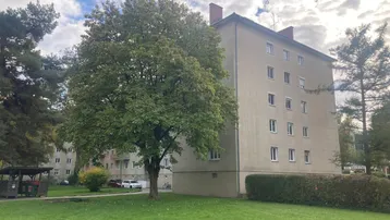 Mehrfamilienhaus mit beiger Fassade, umgeben von Bäumen und einer Grünfläche.
