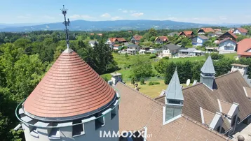 Detailansicht des Schlossturms und Daches mit weitem Blick über die grüne Landschaft und Berge.