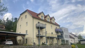 Mehrfamilienhaus mit mehreren Balkonen und einem Carport unter blauem Himmel.