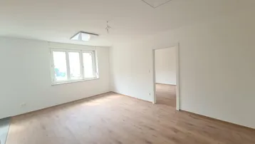 Helles, leeres Zimmer mit Laminatboden und weißen Wänden, bereit zur individuellen Gestaltung.