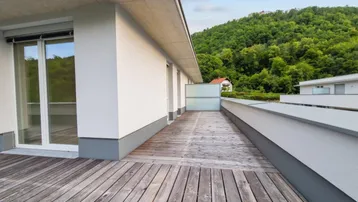 Geräumige Dachterrasse mit Holzboden und weitem Blick ins Grüne und auf bewaldete Hügel.