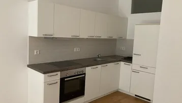Funktionale Küche mit weißen Schränken, dunkler Arbeitsplatte und integrierten Geräten.