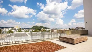 Große Dachterrasse mit weitem Blick über die Stadt und begrünter Fläche unter blauem Himmel.