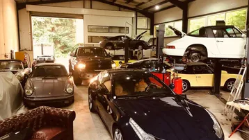 Geräumige Werkstatt mit mehreren Luxusautos, Hebebühnen und einem Ledersofa, ideal für Fahrzeugliebhaber.