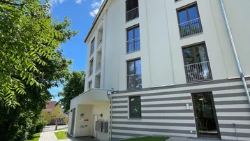 Moderne Gebäudefassade mit Balkonen und gepflegter Grünanlage unter blauem Himmel.