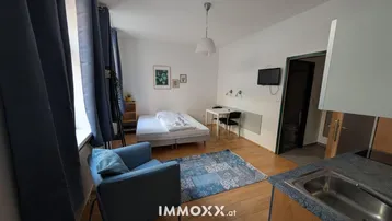 Helles Studio-Apartment mit Schlafbereich, kleiner Küchenzeile und Holzboden.
