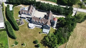 Luftaufnahme des weitläufigen Anwesens mit schlossähnlichem Gebäude und gepflegtem Gartenbereich.