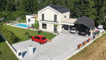 Moderne Villa mit Pool, großem Garten, Carport und Photovoltaikanlage, umgeben von viel Grün.