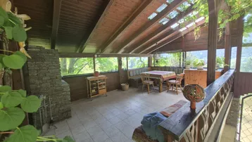 Geräumiger Wintergarten mit Holzdach, Fliesenboden und rustikalem Steinkamin, ideal zum Entspannen.