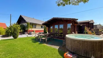 Gartenbereich mit Holzhaus, Whirlpool, Rasenfläche und Sitzgelegenheiten unter blauem Himmel.