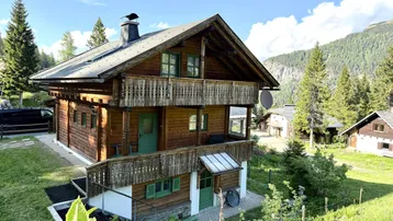 Traditionelles Holzchalet mit Balkonen und Satteldach, eingebettet in eine alpine Berglandschaft mit viel Grün.