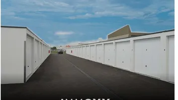 Lange Reihe weißer Garagenboxen entlang einer asphaltierten Zufahrt unter blauem Himmel.