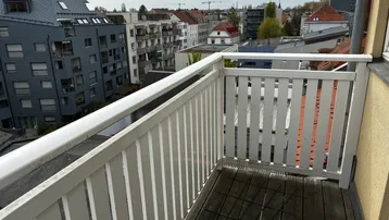 Kleiner Balkon mit Holzboden und weißem Geländer, bietet einen Blick auf die Stadt.