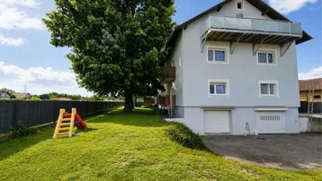 Großzügiger Gartenbereich mit Rasenfläche und Kinderrutsche neben dem Mehrfamilienhaus.