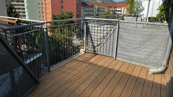 Geräumiger Balkon mit Holzboden und Metallgeländer, bietet einen Blick auf die umliegenden Gebäude.