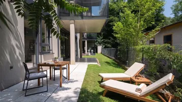 Moderne Terrasse mit Gartenmöbeln und Liegestühlen, umgeben von Grünflächen und Bäumen.